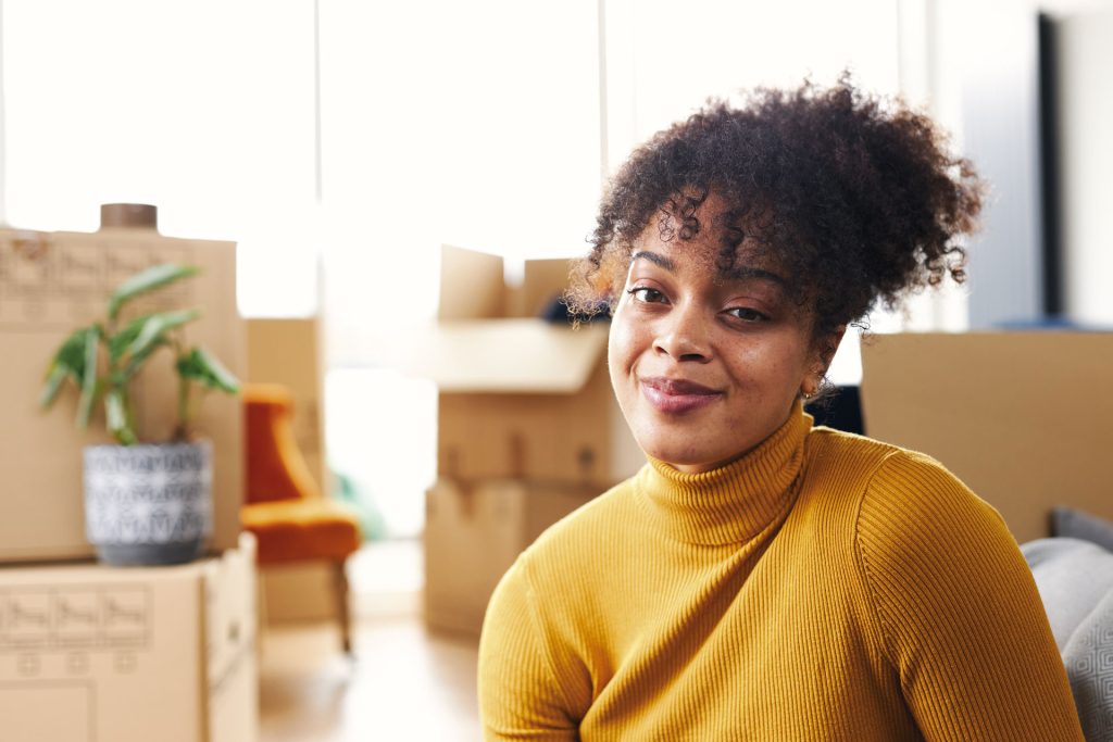 A close up image of a woman sitting between piles of packing boxes.