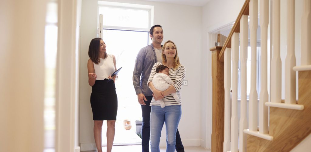 An image of a young couple and their small baby looking at a property with an estate agent.