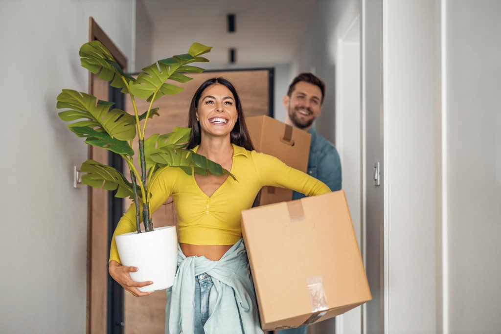 An image of a couple carrying packing boxes and house plants.