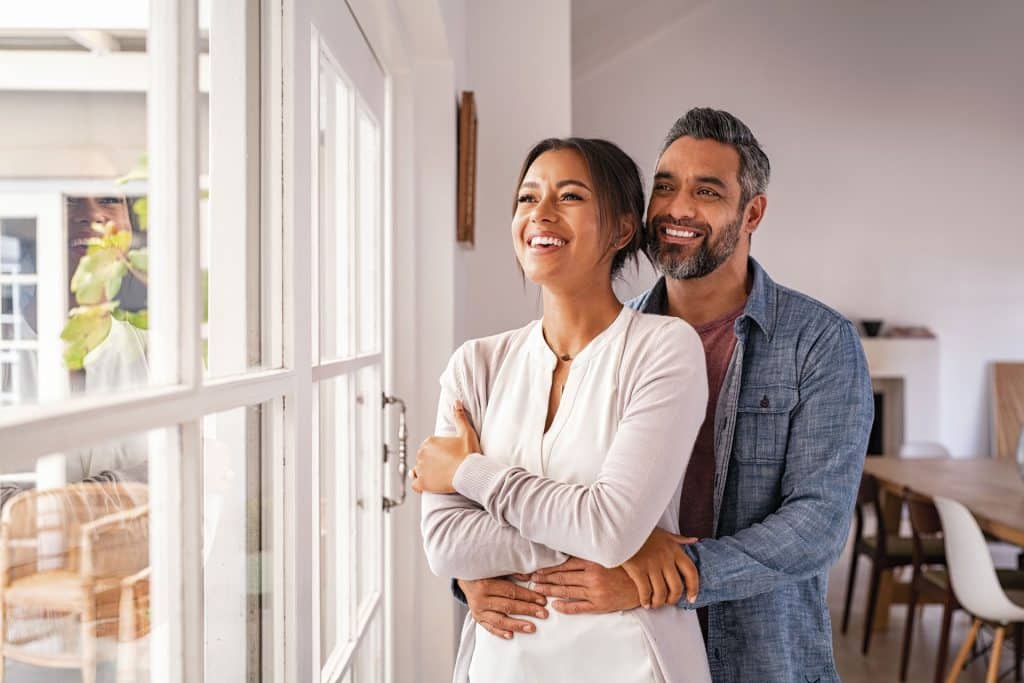 An image of a happy couple hugging while looking out of the window.