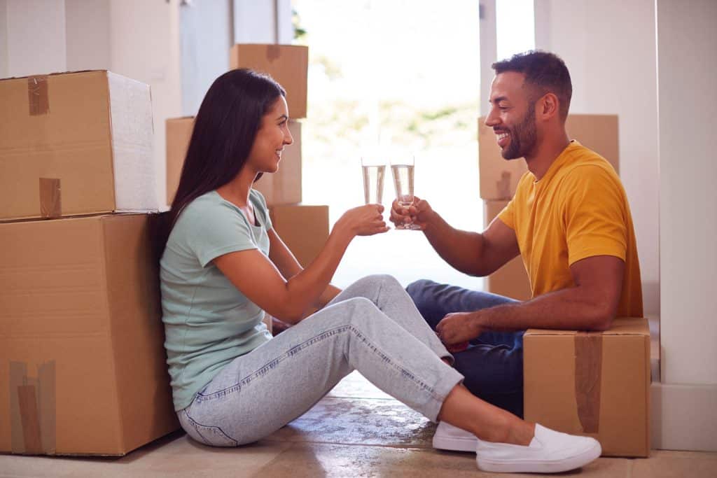 An image of a couple surrounded by moving boxes celebrating with Champagne.