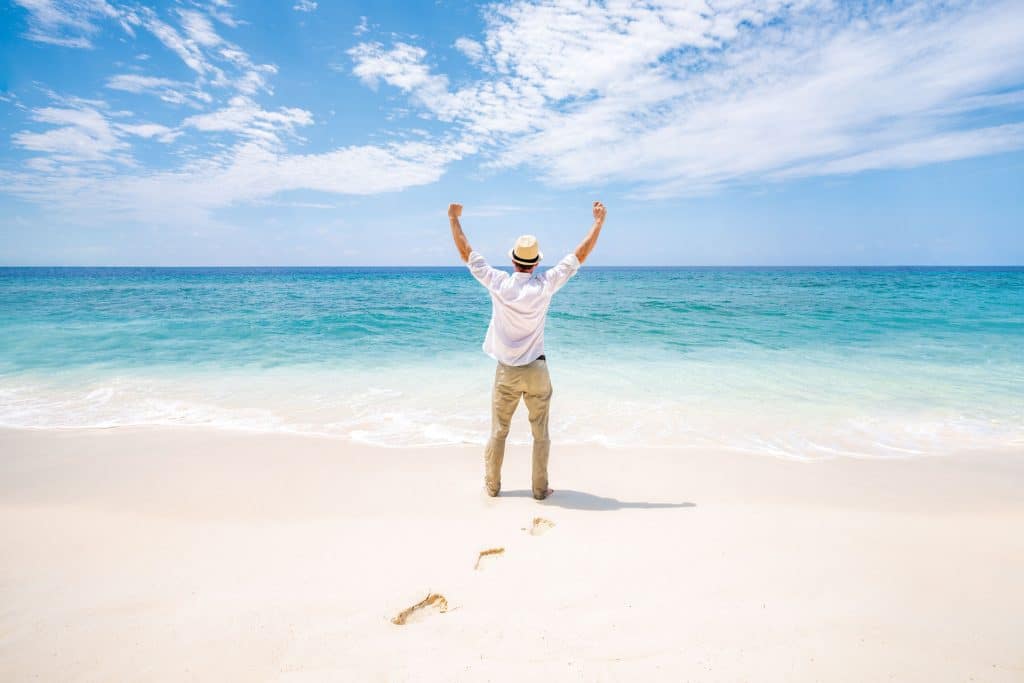 An image of a man on a tropical beach looking out to sea and celebrating.