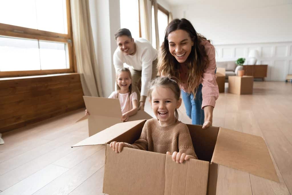 An image of a parents and their two young children playing at home with empty packing boxes.